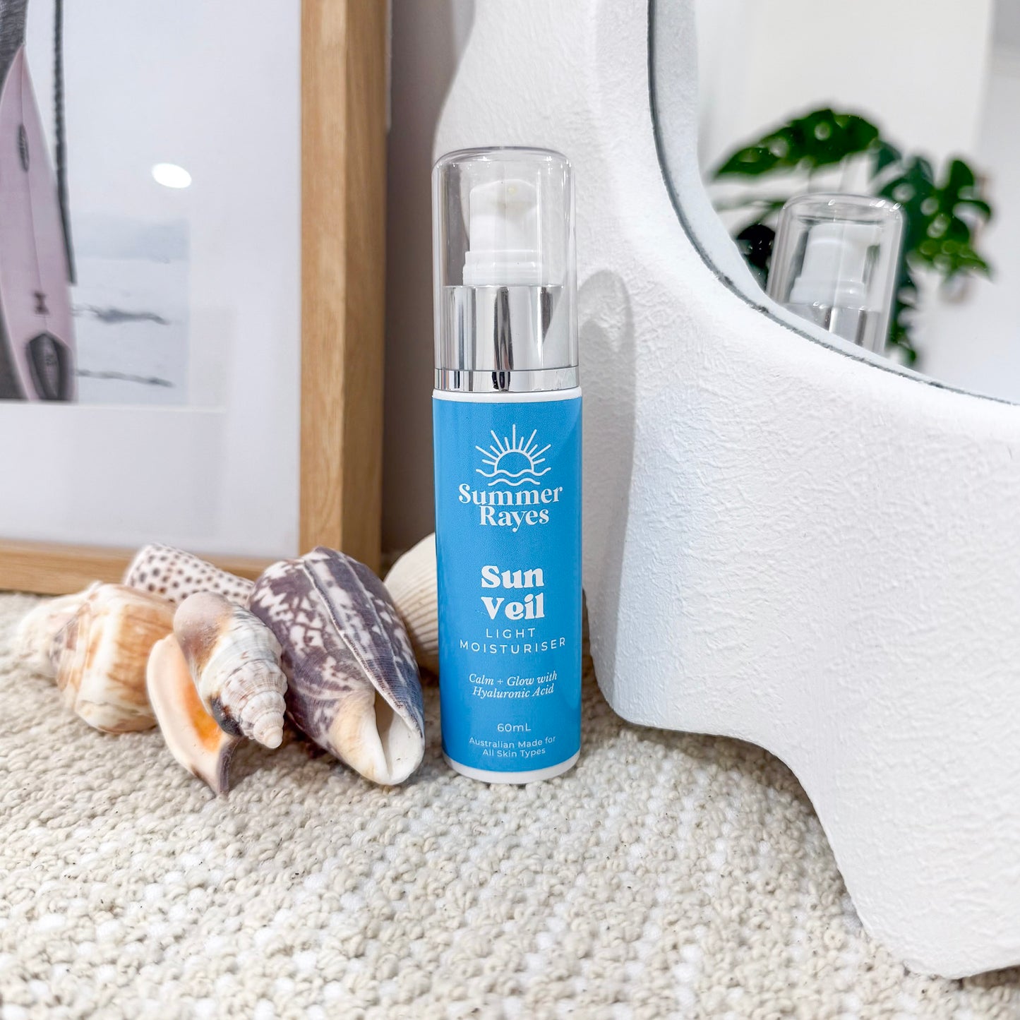 Summer Rayes Sun Veil bottle on a textured surface with seashells and a mirror in the background
