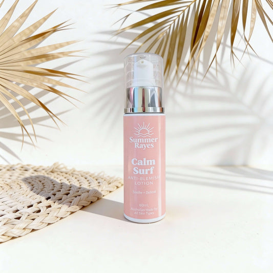 Pink bottle of Summer Rayes Calm Surf lotion on a white surface with palm leaves in the background