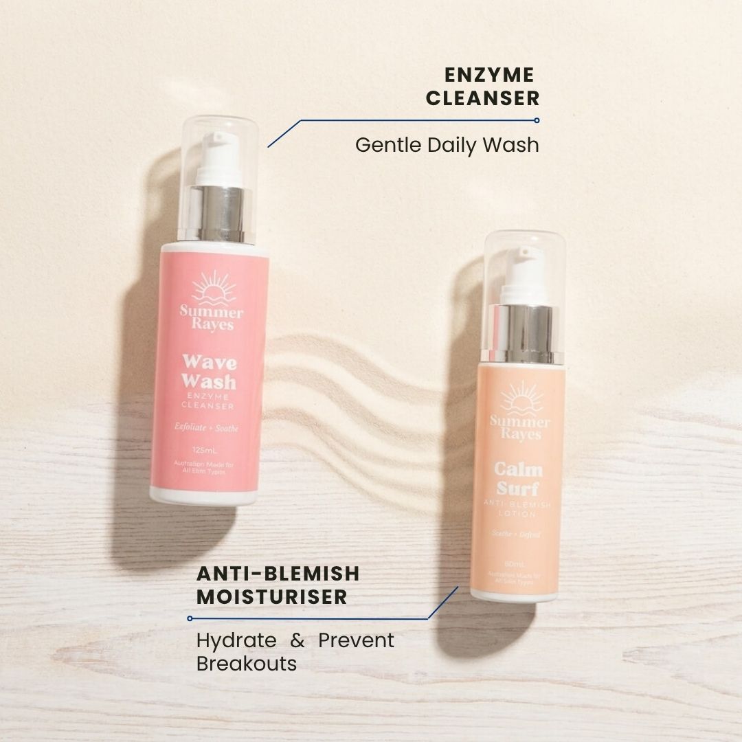 Two Summer Rayes skincare bottles on a light wood background with text labels: 'ENZYME CLEANSER' next to a pink bottle labeled 'Wave Wash' and 'ANTI-BLEMISH MOISTURISER' next to a peach-colored bottle labeled 'Calm Surf'.