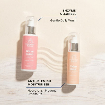 Two Summer Rayes skincare bottles on a light wood background with text labels: 'ENZYME CLEANSER' next to a pink bottle labeled 'Wave Wash' and 'ANTI-BLEMISH MOISTURISER' next to a peach-colored bottle labeled 'Calm Surf'.