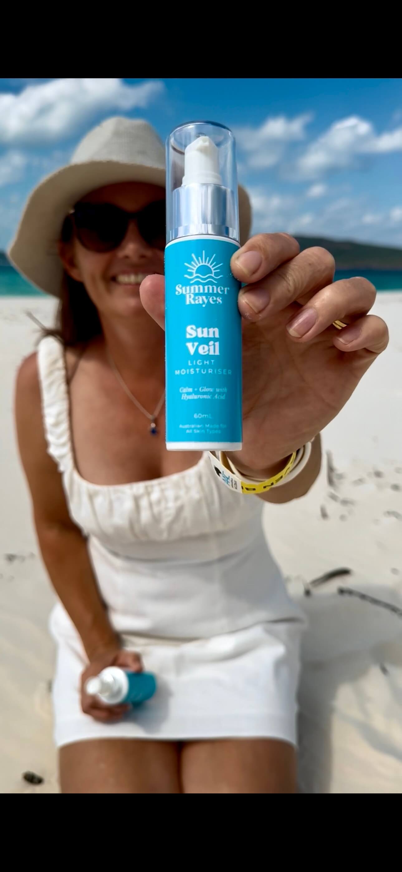 Mum of teens sitting on the beach holding out a teen skincare product from Summer Rayes skincare