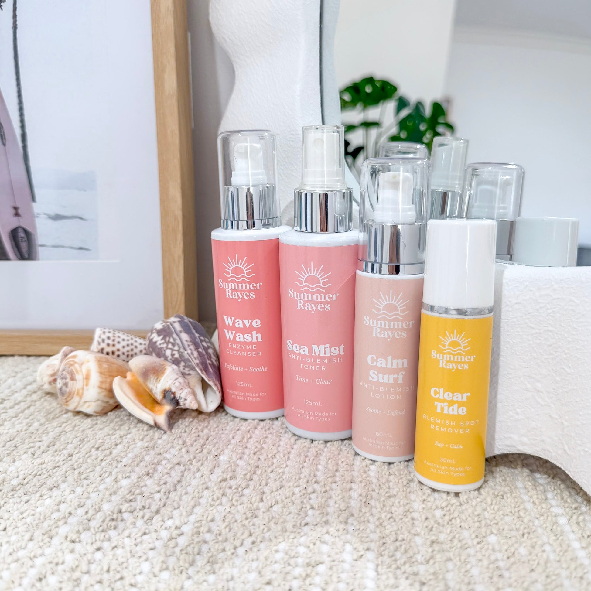 Set of Summer Rayes skincare products on a textured surface with seashells and a framed picture in the background.