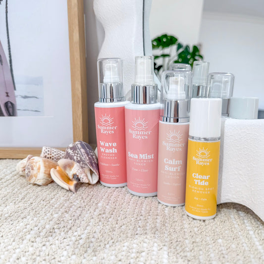 Set of Summer Rayes skincare products on a textured surface with seashells and a framed picture in the background.