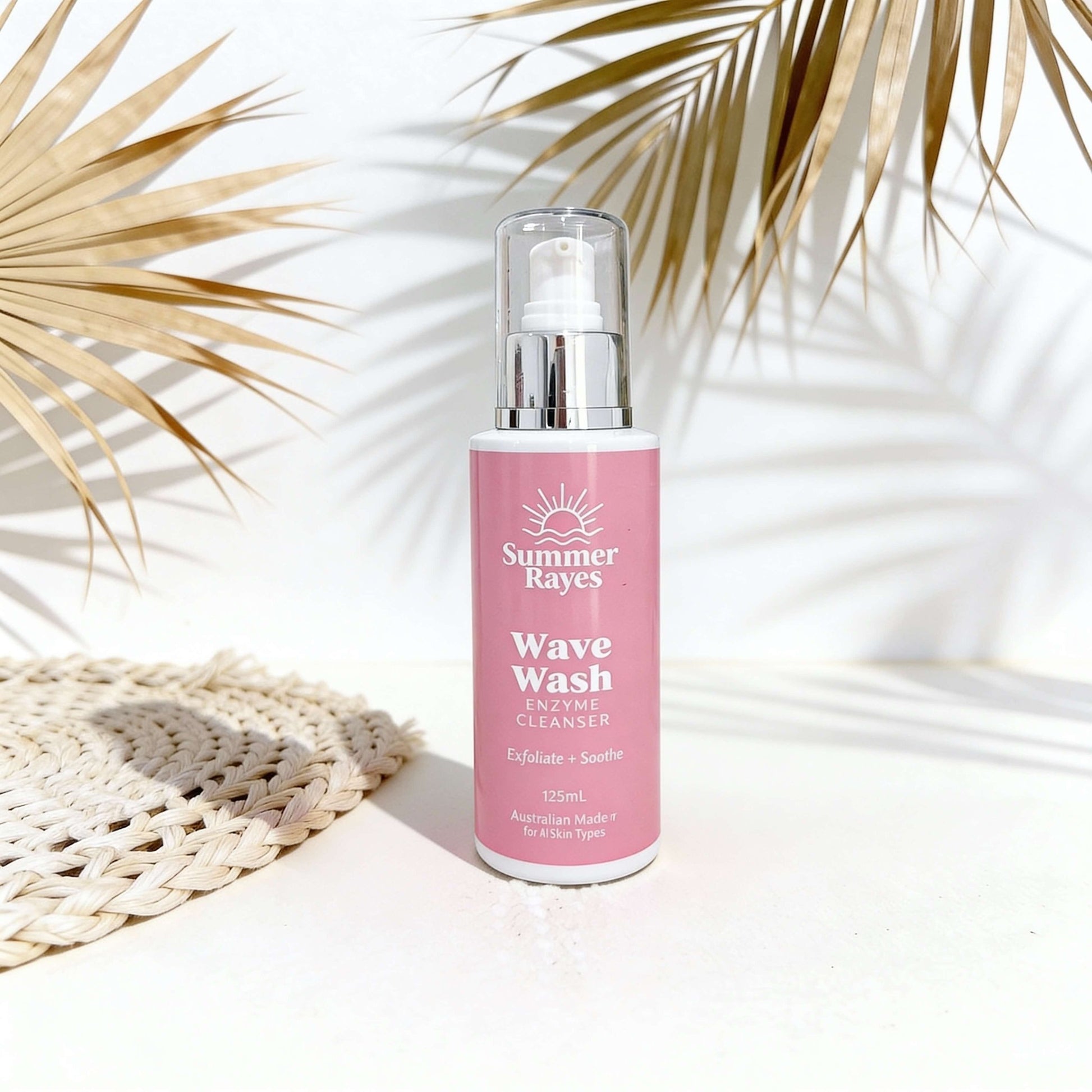 Pink bottle of Summer Rayes Wave Wash with palm leaves in the background