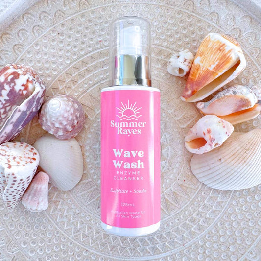 Pink bottle of Summer Rayes Wave Wash teen skincare product with seashells on a textured surface